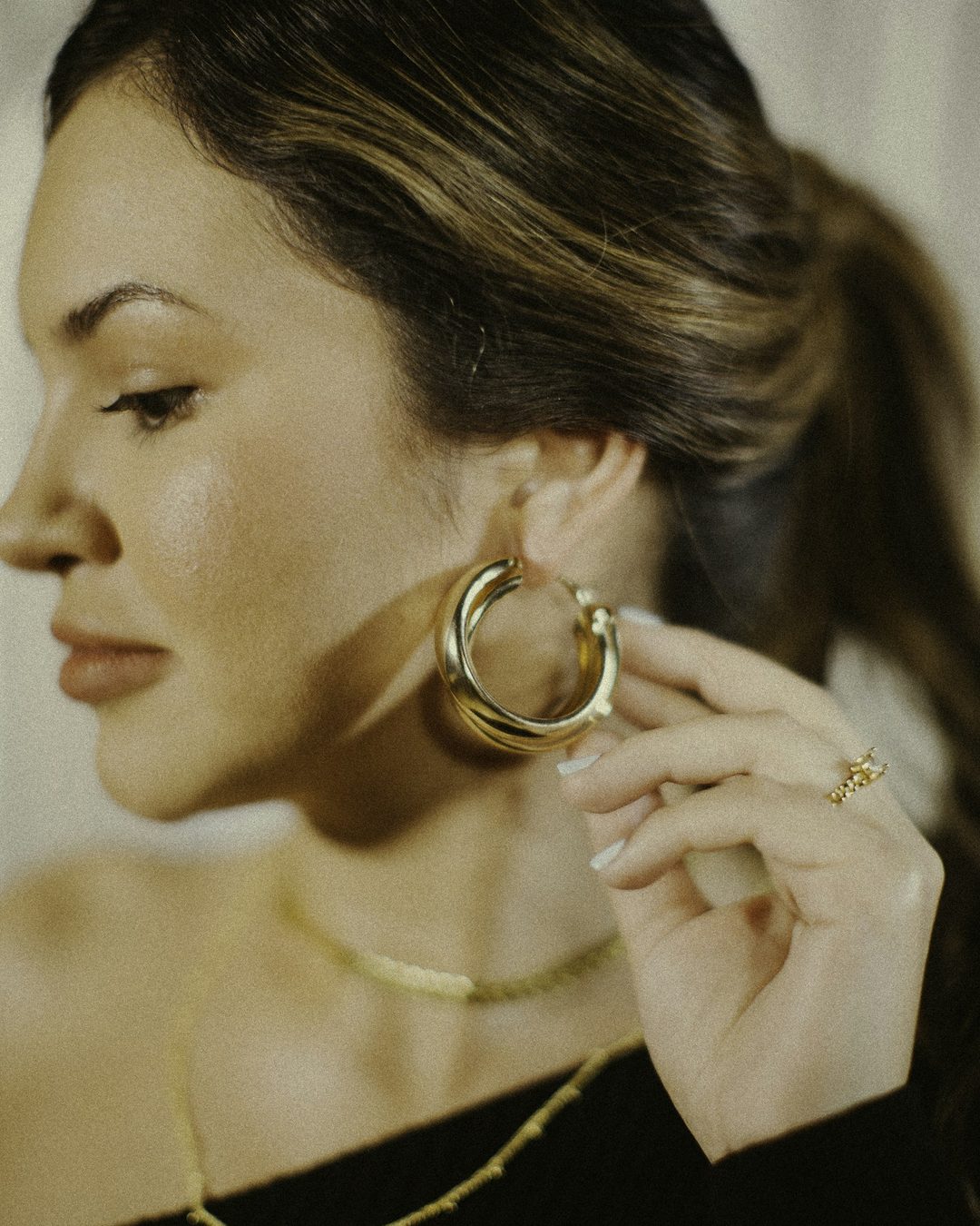 A woman touching a sculpted gold hoop earring in soft light