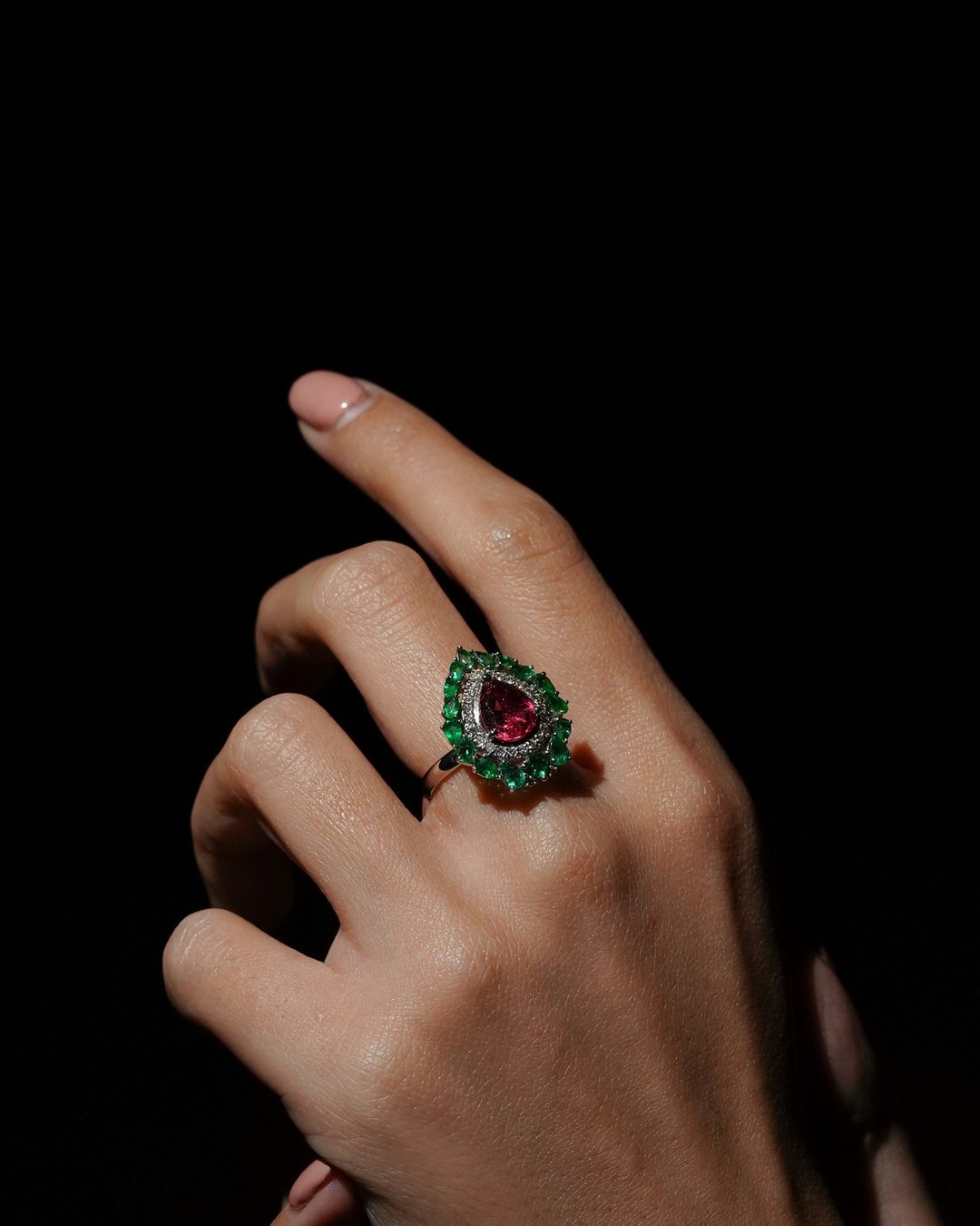 A hand wearing a jewelled cocktail ring against a dark background