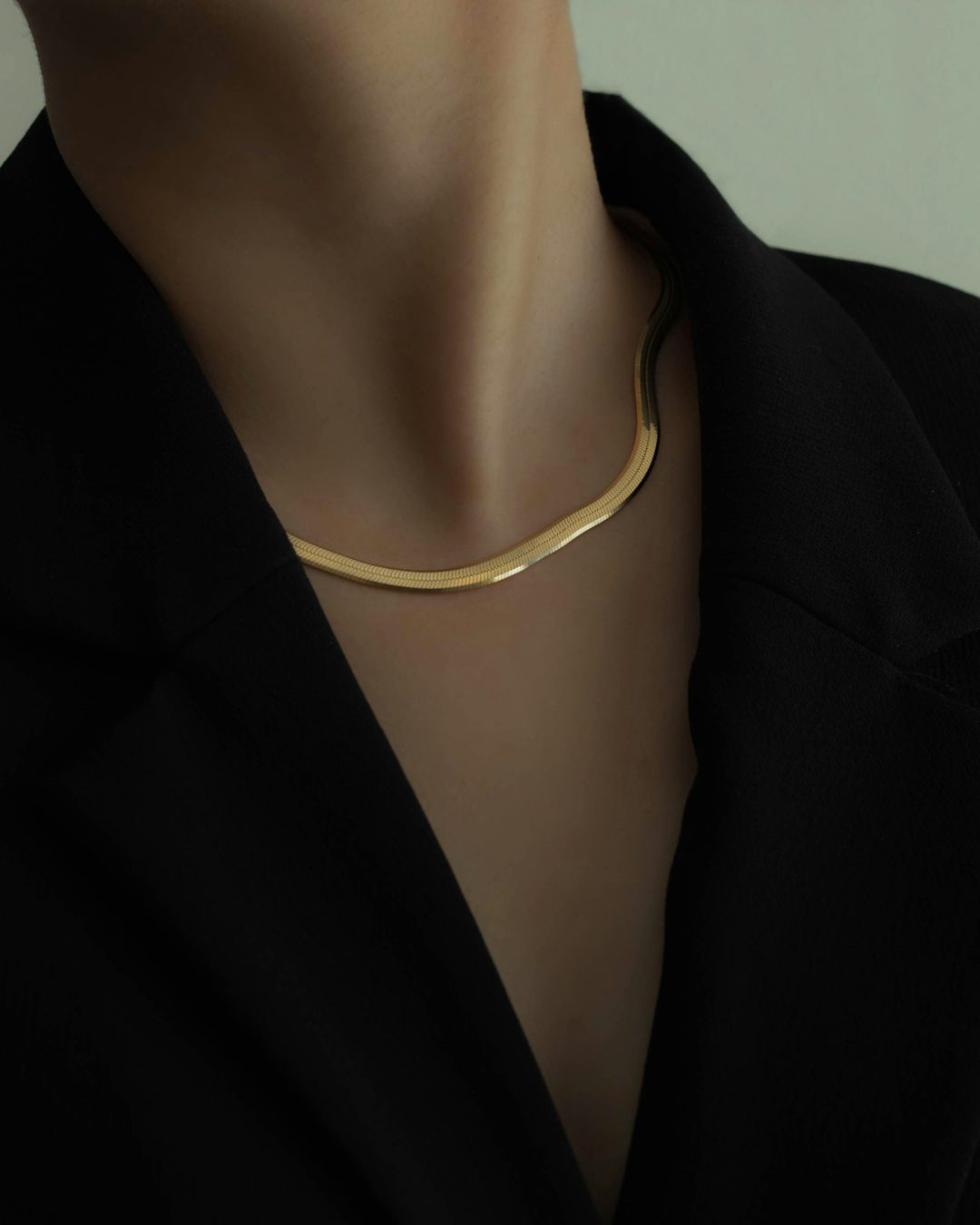 A flat gold chain at the collar of a black blazer