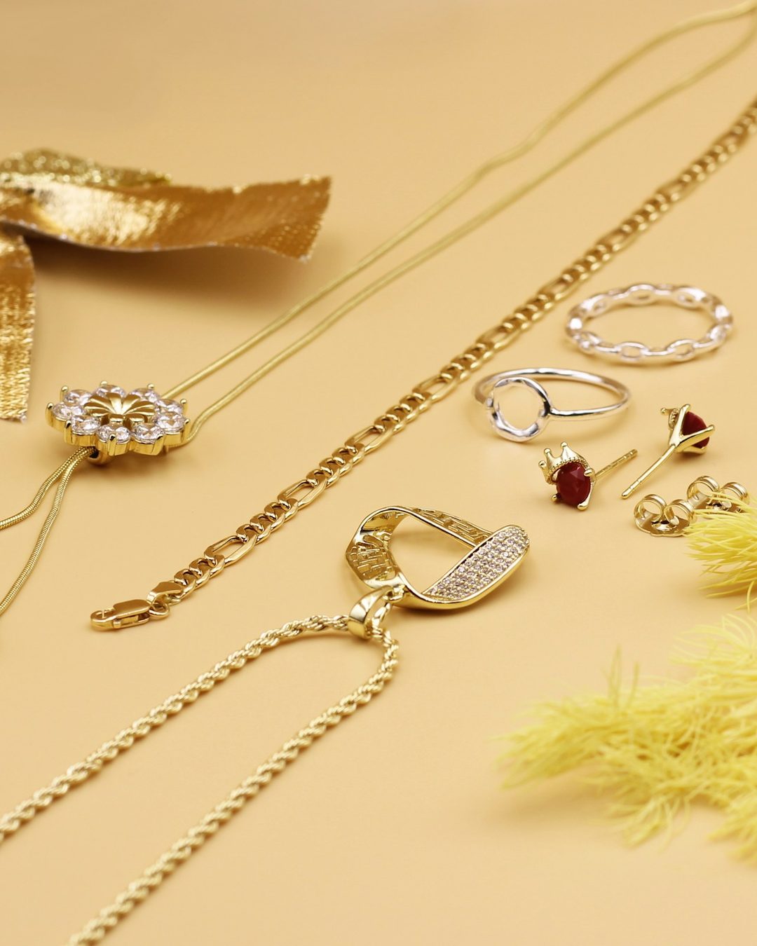 Fine gold chains and earrings laid out on a warm yellow surface